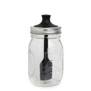 Clear glass mason jar with a black lid and attached silicone brush on a white background