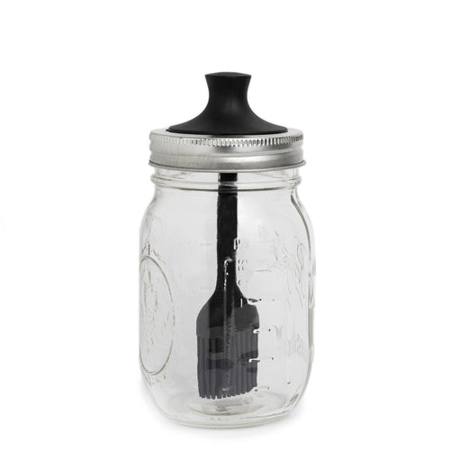 Clear glass mason jar with a black lid and attached silicone brush on a white background