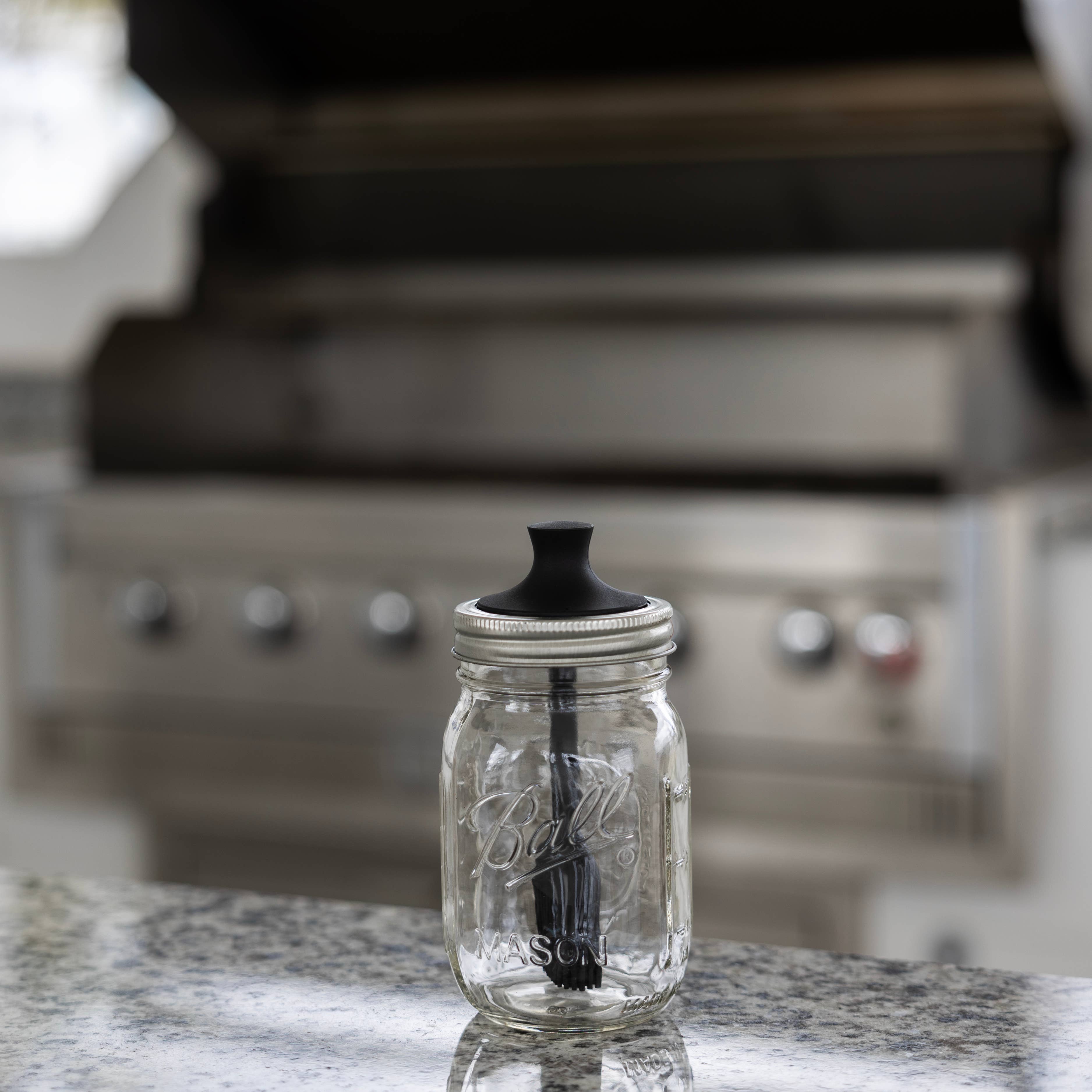 Clear glass mason jar with black lid and silicone brush on a kitchen counter