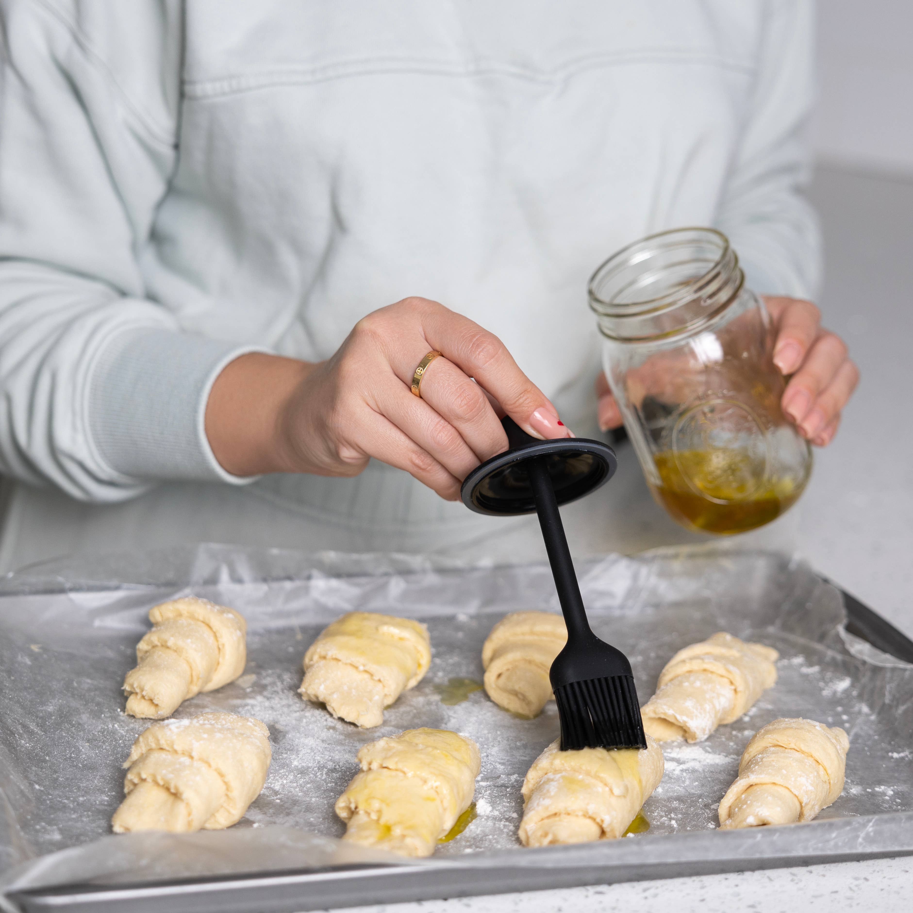Person brushing dough with a brush and oil on a baking sheet
