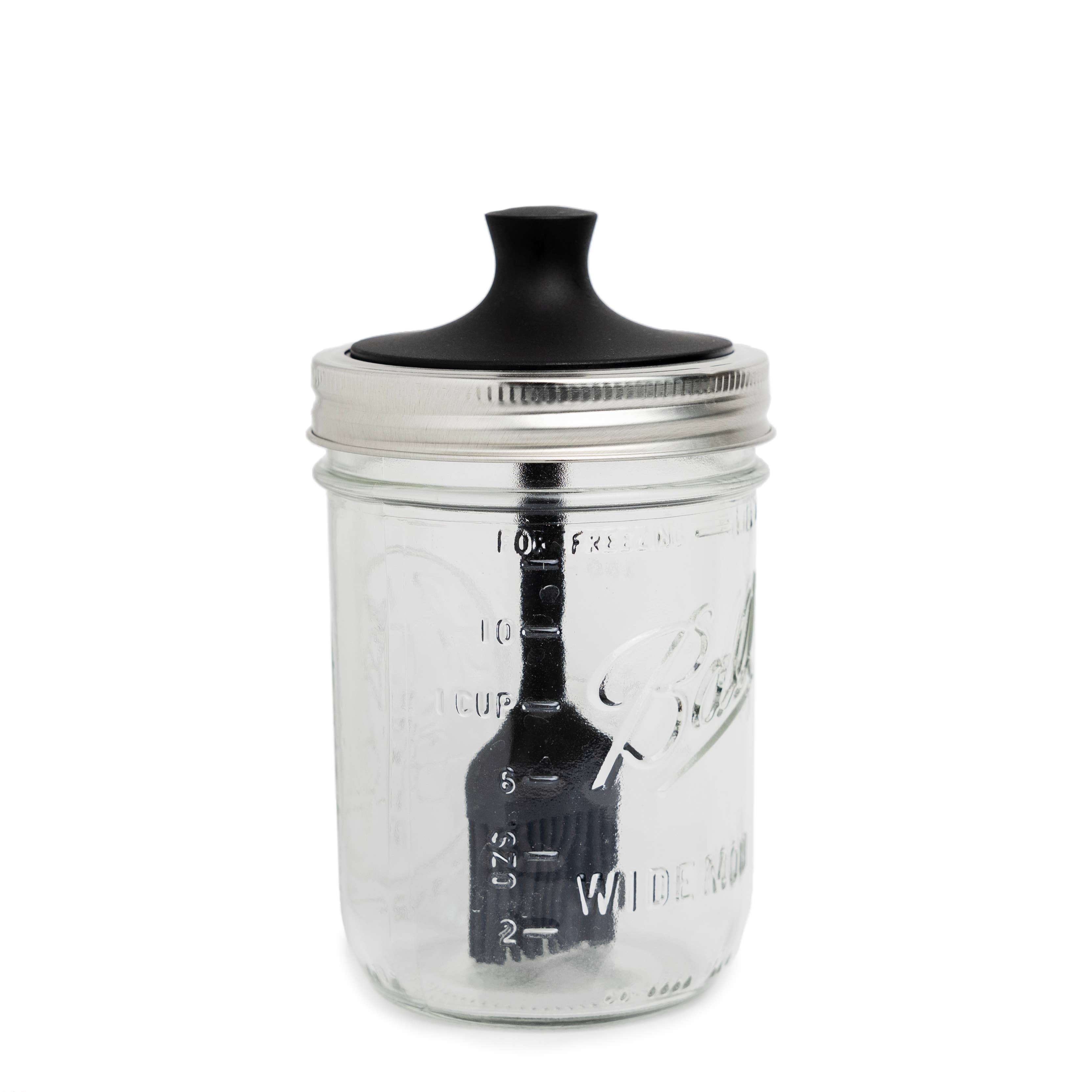 Clear glass jar with black lid and basting brush on a white background