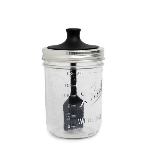 Clear glass jar with black lid and basting brush on a white background