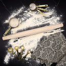 Rolling pin and measuring cups on a surface with flour and a patterned fabric.