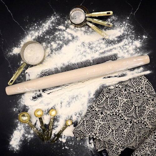 Rolling pin and measuring cups on a surface with flour and a patterned fabric.