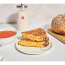 Grilled cheese sandwich on a plate with a bowl of soup and a jar of sourdough in the background.