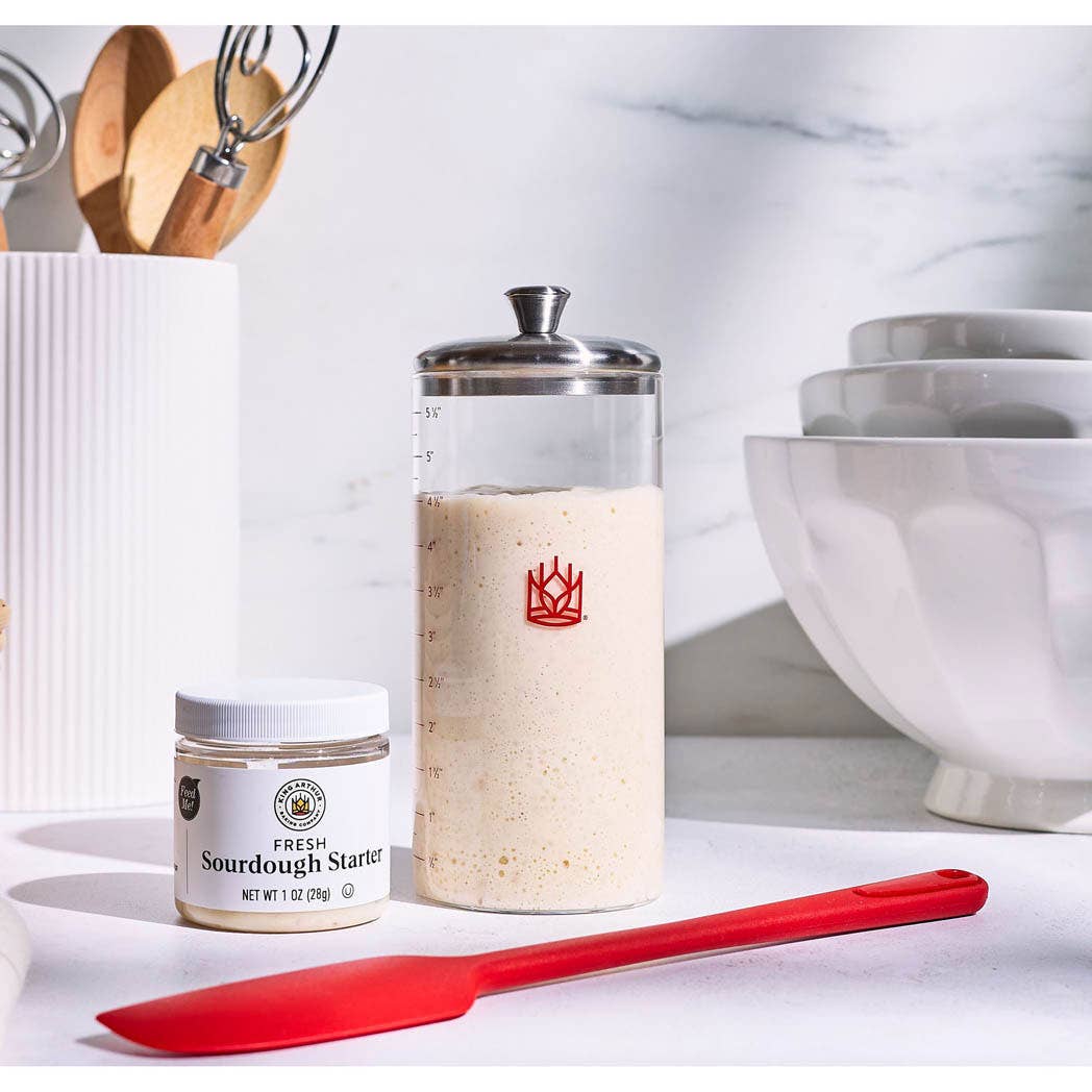 Sourdough starter jar with a red spatula on a kitchen counter.