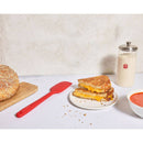 Grilled cheese sandwich on a plate with a jar of sourdough starter and a bowl of soup on a white surface.
