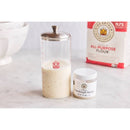 Bowl of dough, jar of sourdough starter, and container of sourdough starter on a marble surface.
