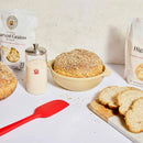 Baked goods including bread and a loaf of bread in a bowl on a white surface with a red spatula.