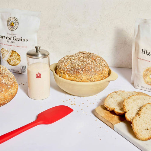 Baked goods including bread and a loaf of bread in a bowl on a white surface with a red spatula.