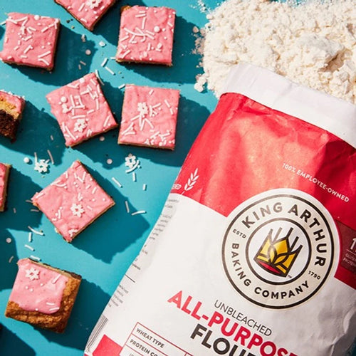 Pink frosted cookies with sprinkles and a King Arthur Flour bag on a blue background