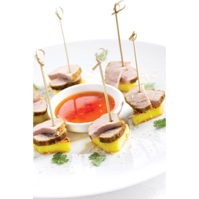 Small appetizers with toothpicks on a white plate with a small bowl of red sauce.