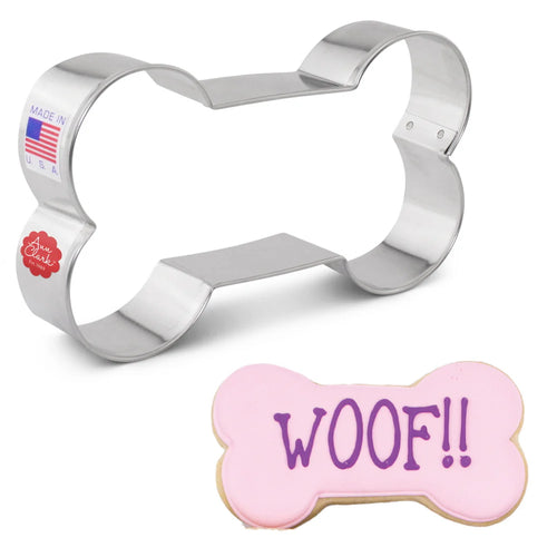 A large dog bone-shaped cookie cutter with a 'WOOF!' text cookie in front, indicating the product is used for cutting shapes in cookies or other food items.