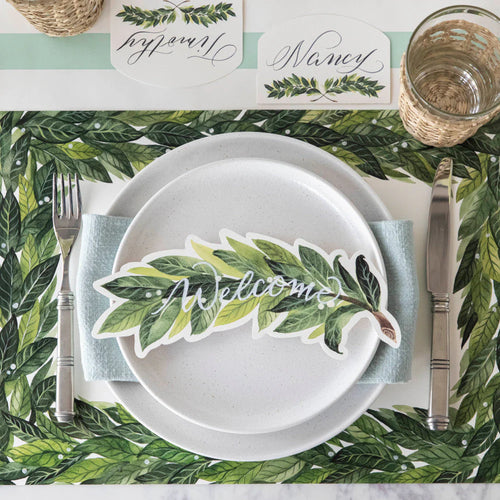 Place setting with a 'Welcome' card on a leaf-patterned tablecloth.