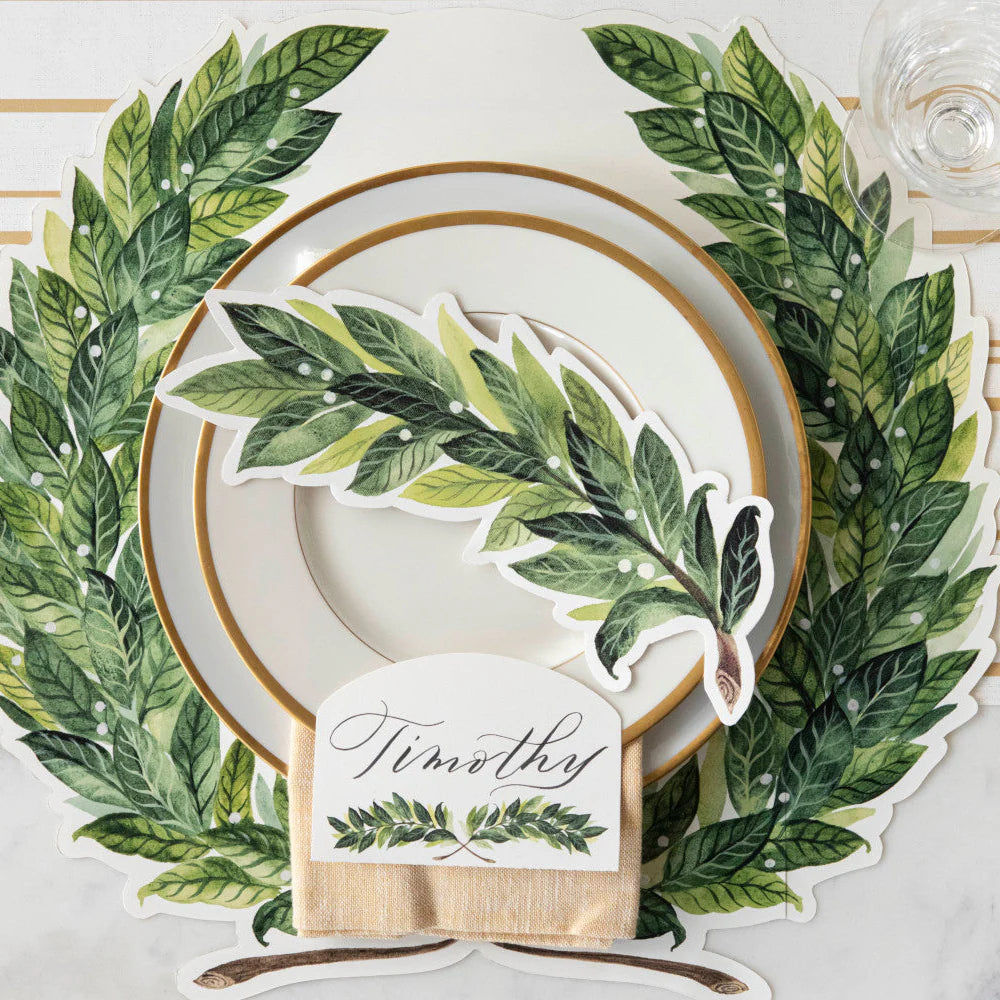 Table setting with green laurel leaf design, white plate, gold rim, and name card.