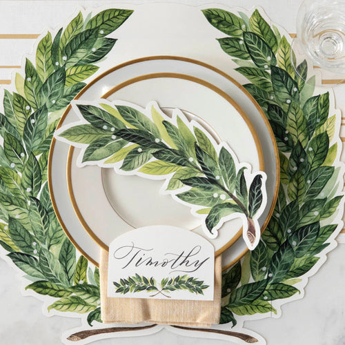 Table setting with green laurel leaf design, white plate, gold rim, and name card.