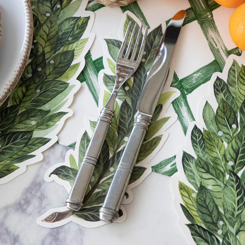 Silver fork and knife on a laurel leaf-patterned placemat with oranges in the background