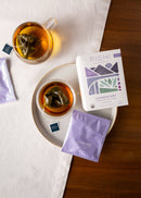 Rishi Lavender Mint tea packaging with two cups of tea and loose tea leaves on a wooden surface.