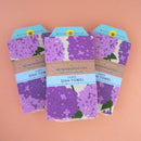 Three lilac dish towels in their packaging on a peach background.