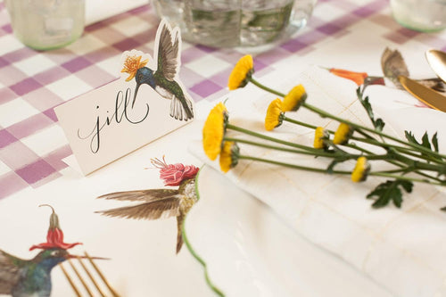 Table setting with yellow flowers, decorative cards, and cutlery on a checkered tablecloth.
