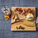Wooden cutting board with prosciutto, cheese, pears, crackers, and a glass of iced tea on a blue fabric background.