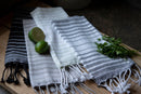 Striped towels with fringe on a wooden surface with limes and herbs.