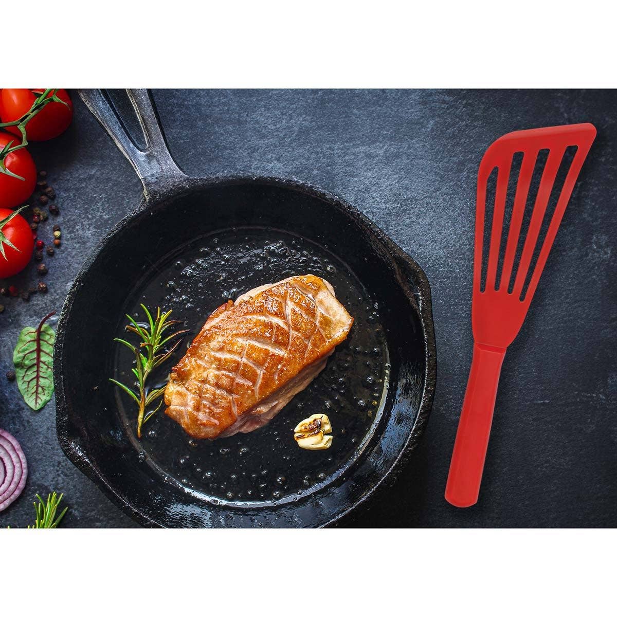 Seared fish in a black skillet with a red fish spatula on a dark surface