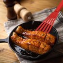 Salmon fillets in a cast iron skillet with a red fish spatula on a wooden surface.