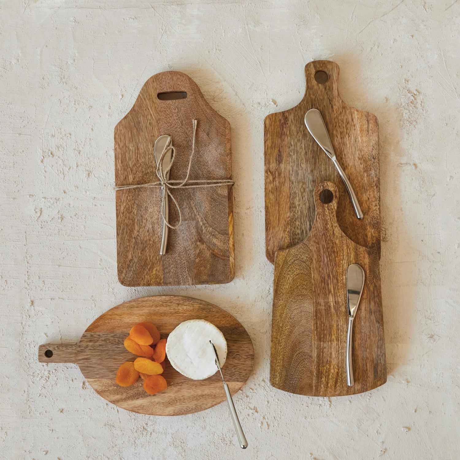Four mango cheese and cutting boards on a rustic white background, one with apricots and cheese and the others with canape knives on them.