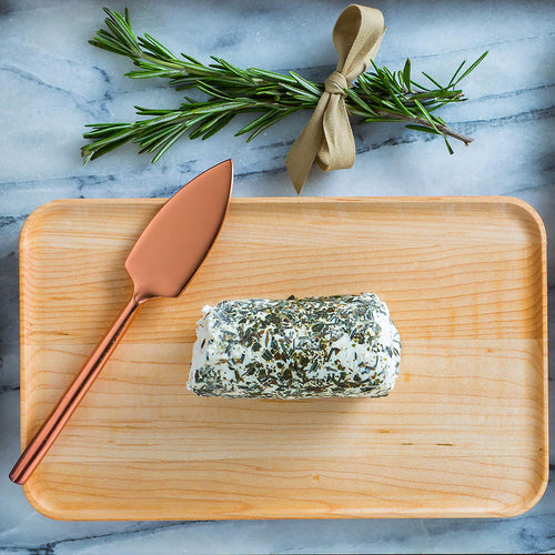 Rolled herb cheese on a wooden board with a copper knife and rosemary on a marble background
