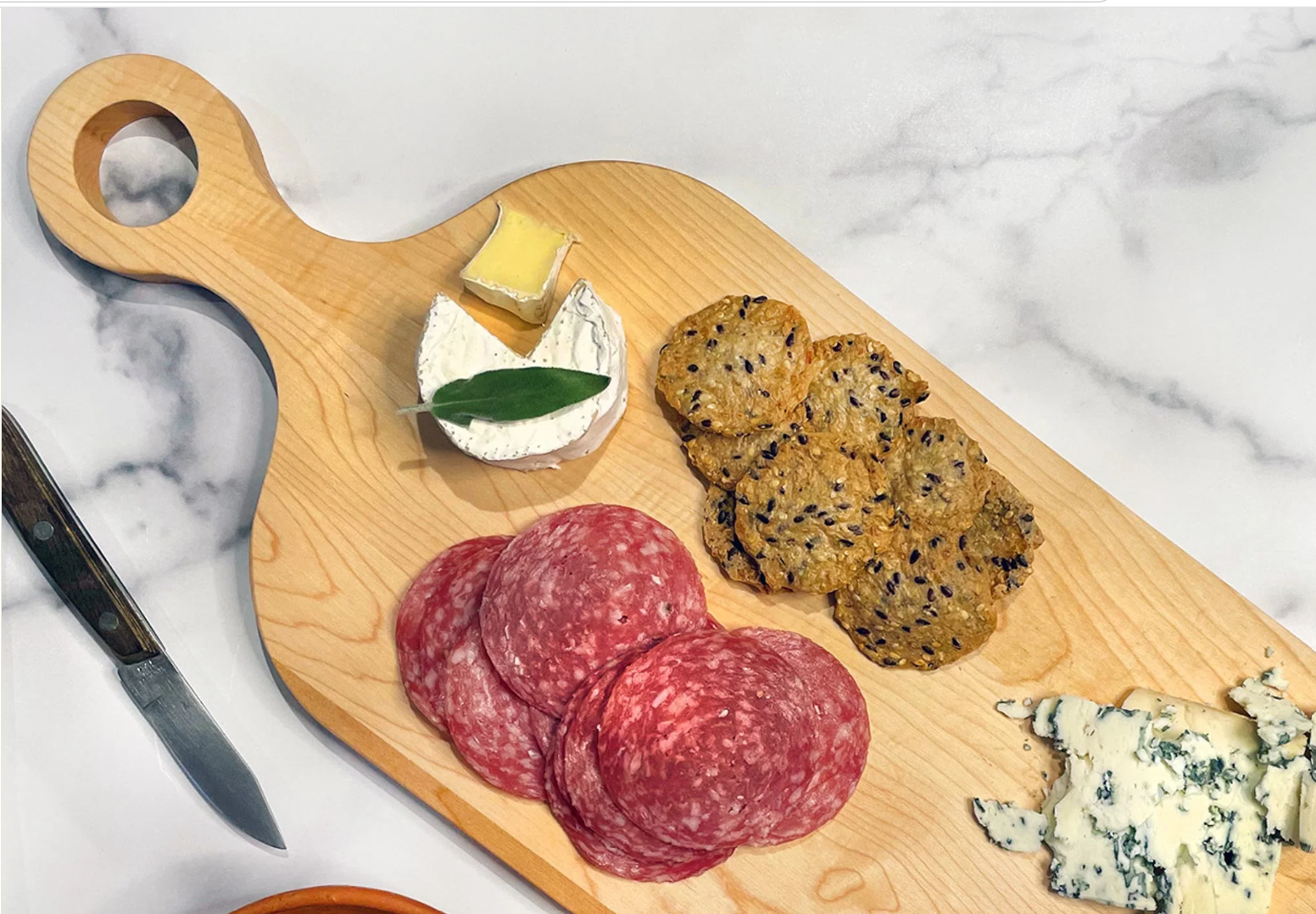 Wooden cutting board with sliced salami, blue cheese, and crackers on a marble surface.