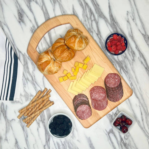 Wooden charcuterie board with croissants, cheese, salami, and fruits on a marble surface.