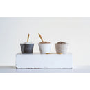 Three small round marble bowls with brass spoons, one with dark marble and two with a lighter marble finish, placed on a white surface.