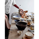 Person preparing food at a wooden table with various bowls and utensils.