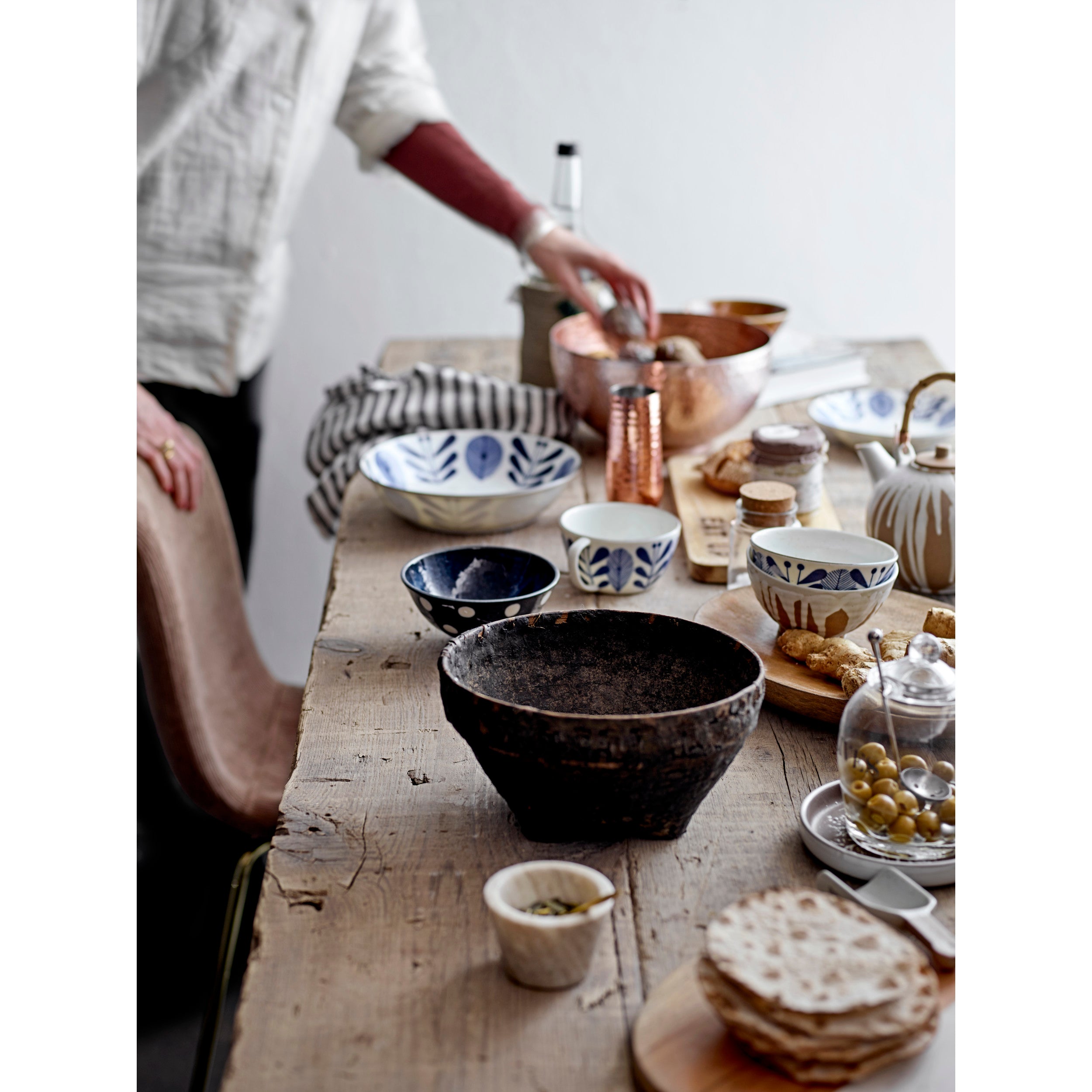 Person preparing food at a wooden table with various bowls and utensils.