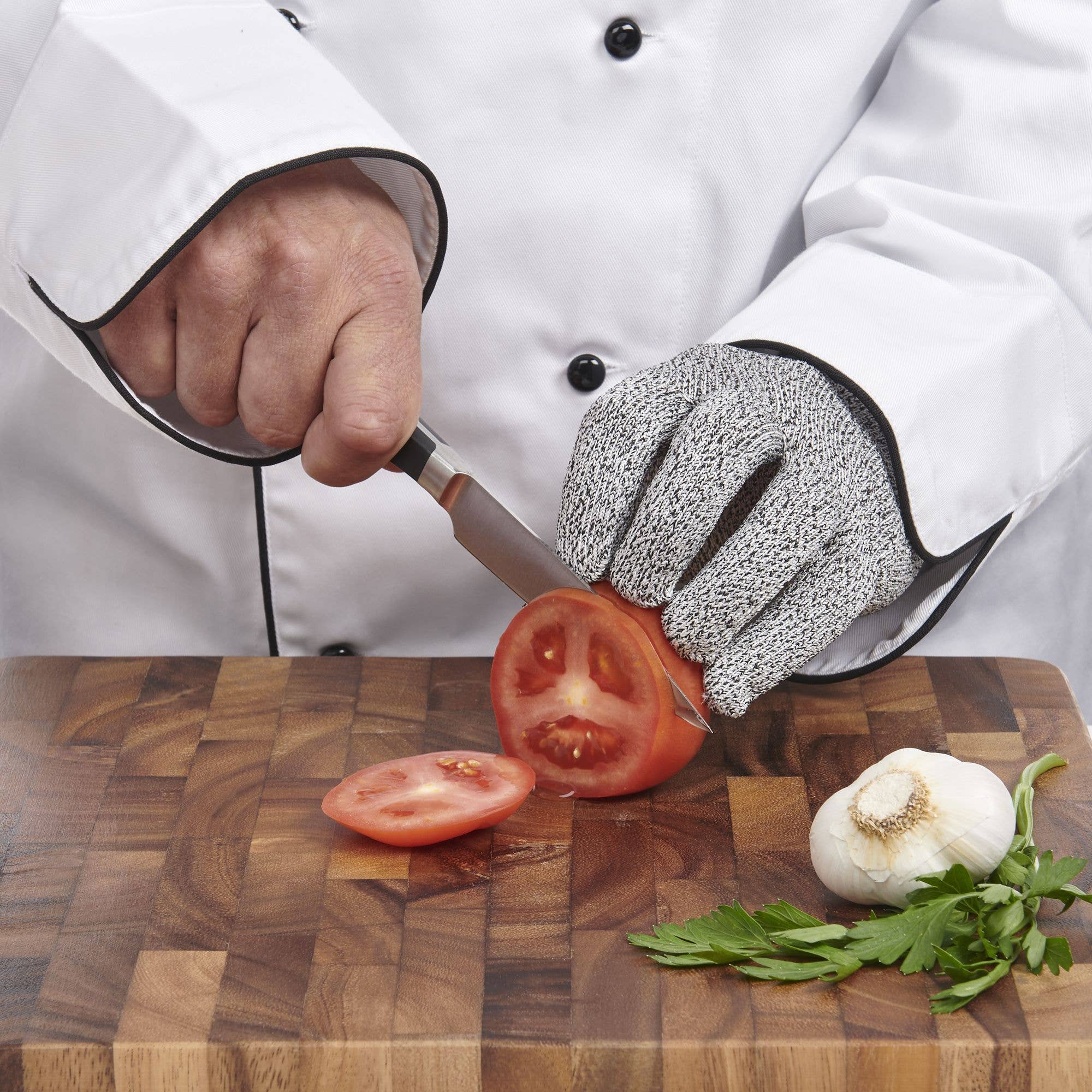 Chef cutting tomatoes on a wooden board with protective glove