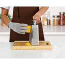 Person wearing a mesh cutting glove while grating cheese with a box grater on a wooden cutting board in a kitchen.