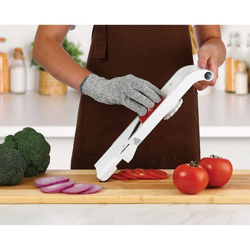 Person wearing a mesh cutting glove using a mandolin slicer on a kitchen counter with vegetables.