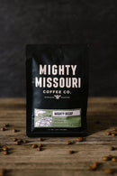 Mighty Missouri Coffee Co. package on a wooden surface with coffee beans around