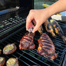 A person using a mini thermometer in meat outside on a grill.
