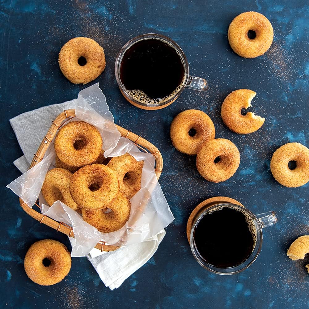 Donuts in a basket and scattered on a blue surface with two cups of coffee.