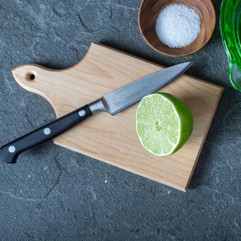 Knife on a wooden cutting board with a halved lime and salt in the background
