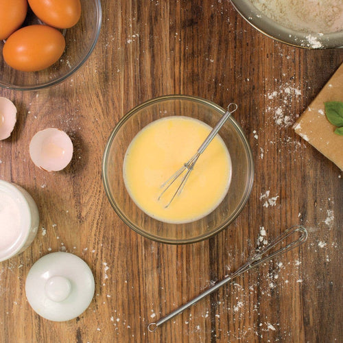 Glass bowl with whisked eggs on a wooden surface with eggs and flour around