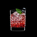 A clear elixir drinking glass with a textured design, filled with a red liquid and garnished with a mint leaf and blueberries.