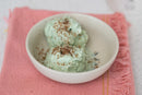Two scoops of green ice cream topped with mocha vanilla sea salt in a white bowl on a pink cloth