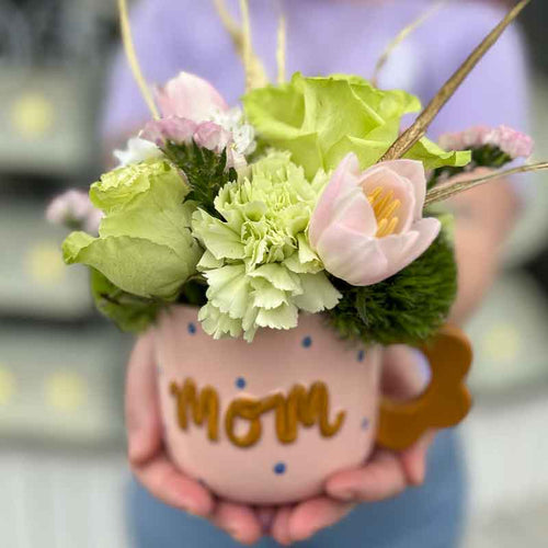 Person holding a mug with flowers and 'mom' written on it