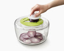 Hand using a salad spinner with sliced onions inside on a white background