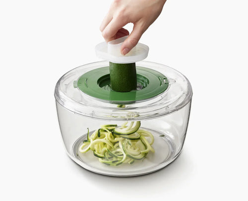 Hand using a spiralizer to create zucchini noodles on a white background