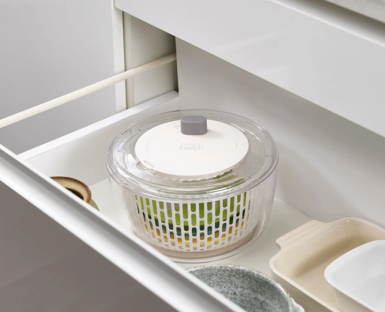 Clear salad spinner with components inside of it set in a white drawer.