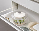 Clear salad spinner with components inside of it set in a white drawer.